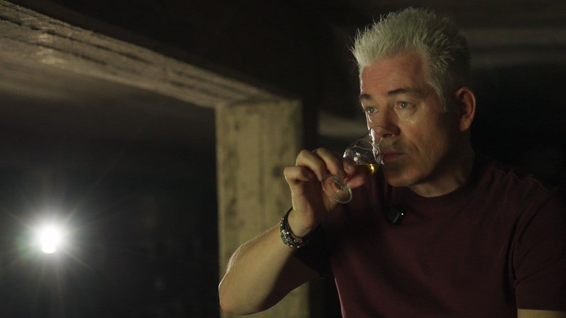 Michael Mittermeier annusa un bicchiere di whisky nel magazzino delle botti di St. Kilian Distillers