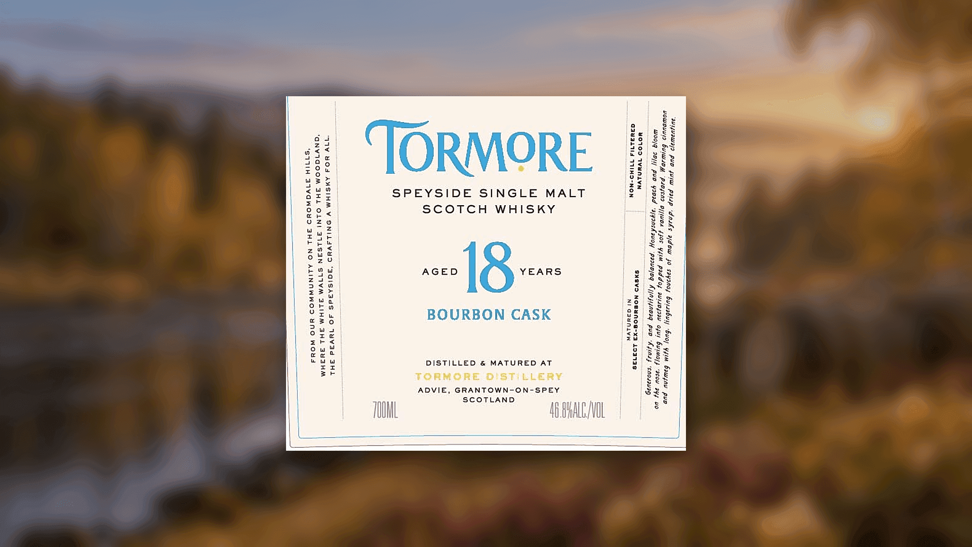 Das Front Etikett des Tormore Aged 18 Years Bourbon Cask vor einer weichgezeichneten Landschaft am River Spey bei Sonnenaufgang